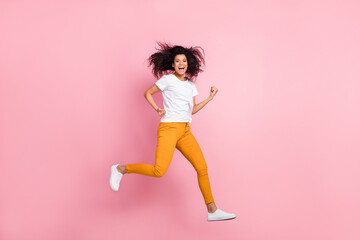Wall Mural - Photo of pretty lucky dark skin lady wear white t-shirt jumping high rising fists screaming isolated pink color background