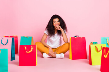 Poster - Full body photo of optimistic curly hairdo young lady sit with bags wear white t-shirt trousers isolated on pink color background