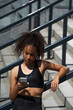 African american sportswoman in earphones using smartphone outdoors