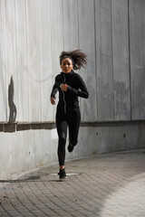 Pretty african american runner near building with concrete facade