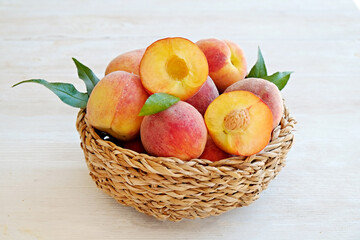 Wall Mural - Bunch of ripe organic peaches in a wicker bowl, white wooden table background. Local produce fruits in a basket. Clean eating concept. Top view, close up, copy space for text.