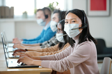 Poster - Young Asian operator in protective mask looking at camera against co-workers