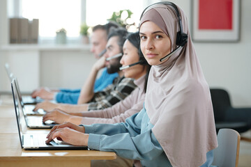 Poster - Young Muslim businesswoman in hijab and headset working in front of laptop