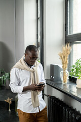 Aufkleber - Young African businessman scrolling in smartphone by office window