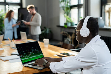Aufkleber - African male economist in headphones using laptop in working environment