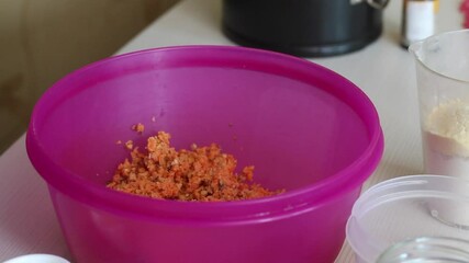 Wall Mural - Cooking carrot cake. A woman pours shredded carrots and walnuts from the blender bowl. Close-up shot.