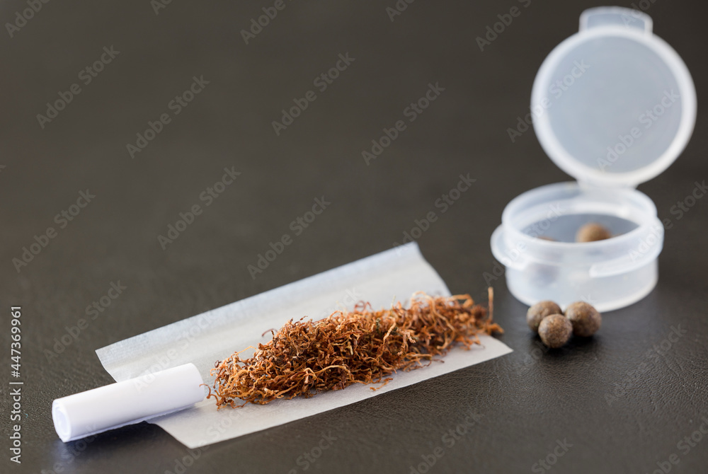 hash with tobacco tobacco on cigarette paper, mouthpiece, hash balls and airtight dispenser,  dark brown background Stock Photo