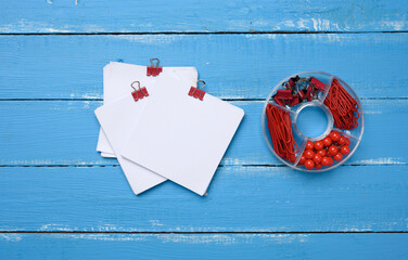 Wall Mural - blank square paper sheets and stationery set with paper clips and clips on blue wooden background