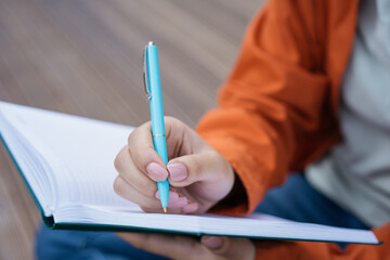 Close up of woman hand holding pen,  taking notes in notepad, writing resume. Author writing a book, selective focus. University student studying, exam preparation, education concept 