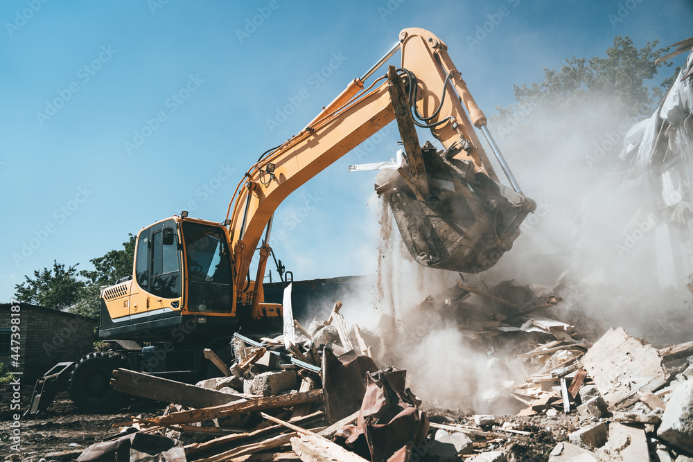 Destruction of old house by excavator. Bucket of excavator breaks concrete structure. - obrazy, fototapety, plakaty 