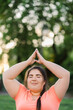 © golubovy - Yoga wellness. Park meditation. Body positive. Harmony balance. Peaceful satisfied obese overweight woman doing upward salute in defocused empty space trees landscape.