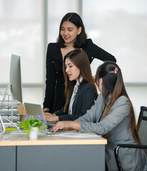 Group of three attractive Asian female office colleagues in formal business suits working together with computer desktop and laptop on the table in office. Concept for modern office working