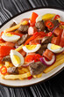 Pique macho is a very popular dish from Bolivia made of beef cuts and fried sausages with fries, eggs, chili peppers and tomatoes closeup in the plate on the table. Vertical.