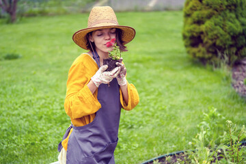 Wall Mural - A young woman gardener is holding a petunia flower in a peat pot