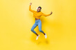Jumping portrait of happy energetic young African American woman wearing headphones listening to music on yellow isolated studio background