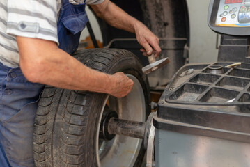 Car mechanic balancing car wheel on a computer machine balancer in auto repair service.