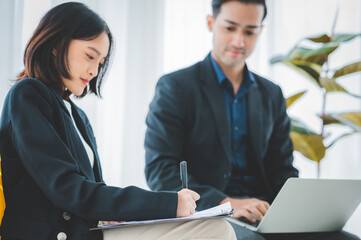 Asian business hold a small meeting inside the office or conference room. Brainstorm to exchange ideas. There are stock boards Laptops and tablets are communication tools. Unity teamwork concept.