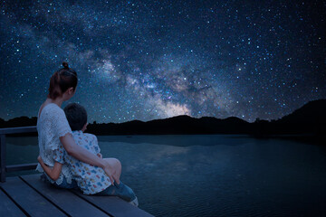 Silhouette mother and child sitting together to hold the view outside the lake. Enjoy the view of the Milky Way on a romantic night.