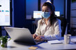 © DC Studio - Close up of businesswoman with face mask checking emails late at night in new normal business office before deadline. Taking notes, analysing documents overtime during global pandemic