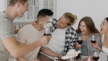 Cheerful Multiethnic Friends Smashing Birthday Cake At Man's Face At Home Party