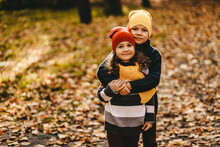 Two Happy Cheerful Children Friends In Warm Clothes Play Together Have Fun Have Fun And Hug Walking Through The Foliage In The Fall Park In Nature Golden Autumn
