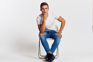 A man sits on a chair in a white t-shirt modern style posing