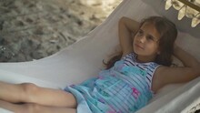 Beautiful Girl Lies In Hammock Sleeping And Dreams. Kid Schoolgirl Rests In Nature With Sea Beach Background