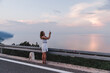 © phpetrunina14 - stop on the road woman taking picture on the phone of sunset above the sea
