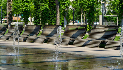 Comfortable benches with climbing Aristolochia plant under pergola. Fountain Three streams turning into complex of fountains in public city park Krasnodar or Galitsky.