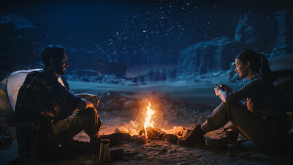 Wall Mural - Happy Couple Sitting by Campfire Watching Night Sky while Camping in the Canyon. Two Traveling people Tell Inspirational Stories at Campsite, Look at Milky Way Stars. On Holiday Vacation Trip