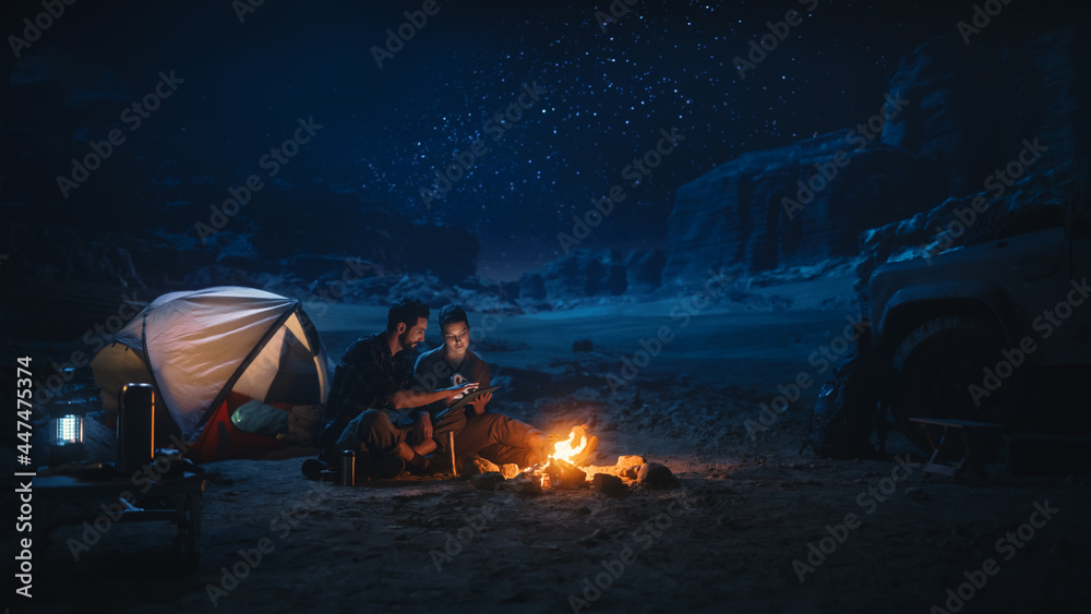 Happy Couple Camping in the Canyon at Night, Use Digital Tablet Computer, Sitting by Campfire. Two Traveling people Have Fun, Smile, Post on Social Media, Watch Funny Videos on Internet - obrazy, fototapety, plakaty 