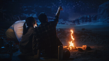 Happy Couple Nature Camping in the Canyon, Sitting by Campfire Watching Night Sky with Milky Way Full of Bright Stars. Two Travelers In Love On a Romantic Vacation Trip. Back View Shot