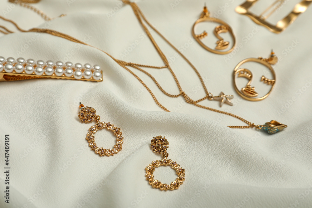 Stylish golden bijouterie on white fabric. Elegant jewelry