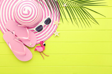 Wall Mural - Straw hat with pair of flip-flops, sunglasses, starfishes and palm leaf on green wooden table