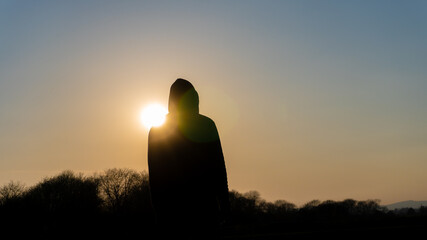 Canvas Print - A moody, hooded figure silhouetted against the sunset. With deliberate lens flare.