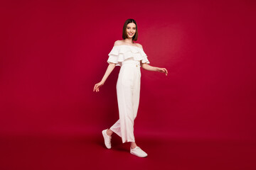 Full length body size photo pretty brunette wearing stylish clothes walking forward isolated red color background