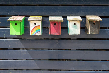 Five colored bird houses on a wooden shed.