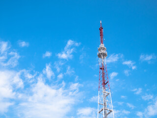 Television high metal tower against the blue sky with white clouds. High metal cellular communication tower with transmitters. TV  antenna.