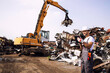 Man controlling process of industrial scrap metal lifting at junk yard.