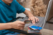 © Anna - Close up image of boy's hands with credit card and big stack of different cards near laptop executing online payment. New reality, convenience on online shopping from home
