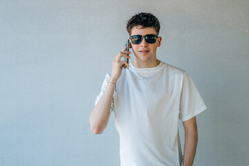 Wall Mural - teen boy with mobile phone and sunglasses isolated on wall background