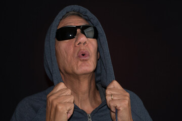 Wall Mural - Older man wearing a dark hoodie and shades against a black background