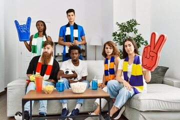 Canvas Print - Group of friends supporting football team watching tv al home sitting on the sofa looking positive and happy standing and smiling with a confident smile showing teeth