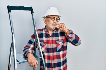 Canvas Print - Handsome mature handyman close to construction stairs wearing hardhat mouth and lips shut as zip with fingers. secret and silent, taboo talking