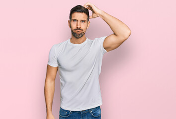 Wall Mural - Handsome man with beard wearing casual white t shirt confuse and wonder about question. uncertain with doubt, thinking with hand on head. pensive concept.