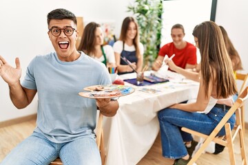 Poster - Young artist man drawing at art studio celebrating victory with happy smile and winner expression with raised hands