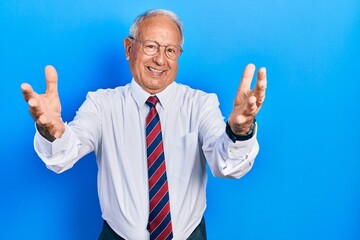 Sticker - Senior man with grey hair wearing business suit and tie looking at the camera smiling with open arms for hug. cheerful expression embracing happiness.