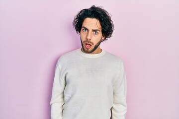 Poster - Handsome hispanic man wearing casual white sweater in shock face, looking skeptical and sarcastic, surprised with open mouth