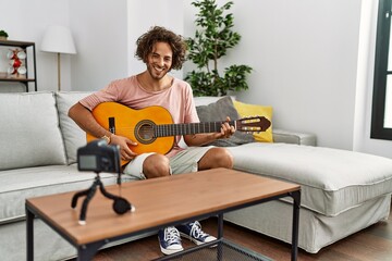 Canvas Print - Young hispanic man recording with camera playing classical guitar at home.