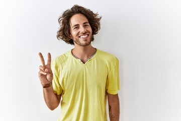 Sticker - Young hispanic man standing over isolated background showing and pointing up with fingers number two while smiling confident and happy.